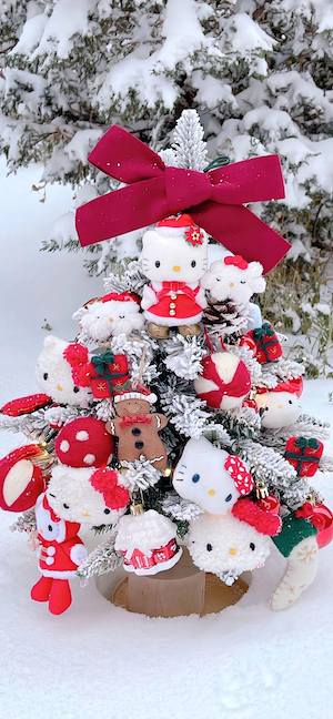 Un pequeño árbol de Navidad cubierto de nieve decorado con peluches de Hello Kitty y un gran lazo rojo.