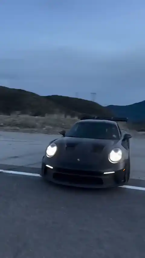 Cinematic shot of a dark Porsche 911 GT3 RS driving on a highway at dusk, animated live wallpaper.