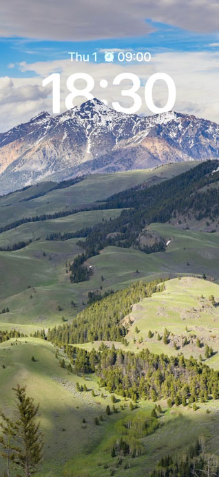 Un paisaje majestuoso con una montaña nevada bajo un cielo azul, colinas verdes y bosques en primer plano para pantalla de móvil.