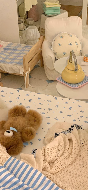 파란 꽃무늬 침대 위에 놓인 갈색 테디베어와 빈티지한 느낌의 방 인테리어.