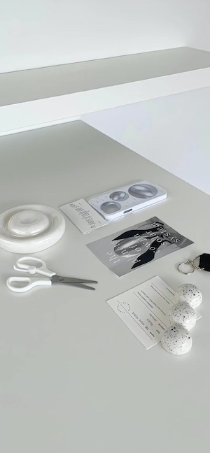 Una superficie blanca con tijeras, tarjetas y esferas decorativas blancas en una composición minimalista.