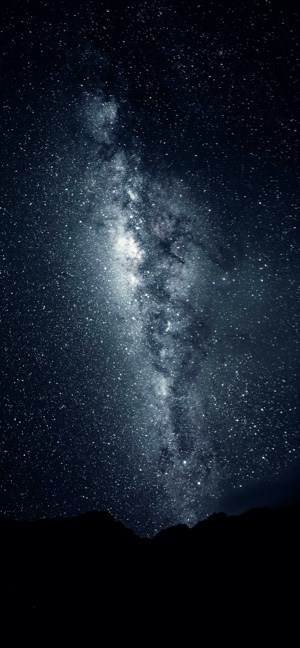 夜晚暗色山脈剪影上方，璀璨的銀河與繁星垂直展開的景象。